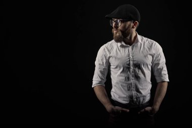 Gözlük sakallı genç bir adam ve bıyıklı bir siyah şapka ve beyaz bir gömlek, bir karanlık studio arka plan portresi
