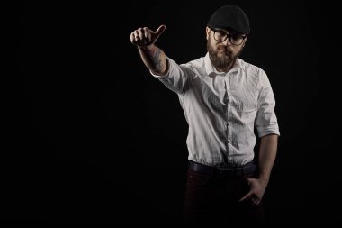 genç yakışıklı adam gözlüklü sakallı ve bıyıklı bir siyah şapka ve beyaz bir gömlek el hareketleri, bir karanlık studio arka plan çeşitli gösterir