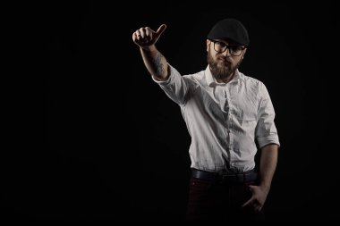 genç yakışıklı adam gözlüklü sakallı ve bıyıklı bir siyah şapka ve beyaz bir gömlek el hareketleri, bir karanlık studio arka plan çeşitli gösterir