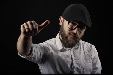 genç yakışıklı adam gözlüklü sakallı ve bıyıklı bir siyah şapka ve beyaz bir gömlek el hareketleri, bir karanlık studio arka plan çeşitli gösterir