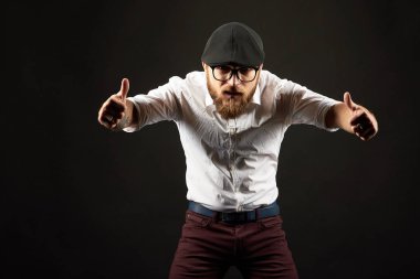 genç yakışıklı adam gözlüklü sakallı ve bıyıklı bir siyah şapka ve beyaz bir gömlek el hareketleri, bir karanlık studio arka plan çeşitli gösterir