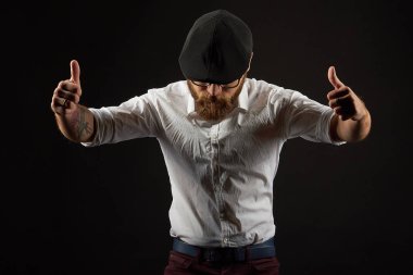 genç yakışıklı adam gözlüklü sakallı ve bıyıklı bir siyah şapka ve beyaz bir gömlek el hareketleri, bir karanlık studio arka plan çeşitli gösterir