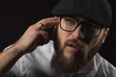 bir sakal ve bir siyah kap ve beyaz bir gömlek bir bıyık ile Gözlük Genç yakışıklı bir adam baş ağrısı gibi kafasına ellerini tutan, karanlık bir stüdyoda