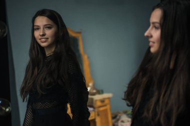 küçük güzel tatlı ve büyüleyici kız tahta büyük ayna yakınında duruyor ve onun yansıma görünür. Rahat gri duvarlara sahip oda