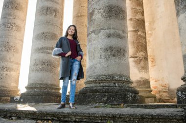 Genç, çekici, uzun saçlı güzel kız eski binanın arkasında, güneşin ilk ışıklarında duran kolye.