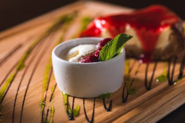 Tahta bir arka planda beyaz dondurma ve ahududu. Yanlarında da bir parça peynirli kek.