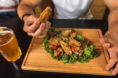 Önündeki masada oturan beyaz tişörtlü, genç, yakışıklı duygusal adam üzerinde leziz kızarmış tavuk kanatları olan ahşap bir tahta, mesaj ya da tasarım için yerleşim yeri, fast food