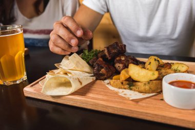 Önündeki masada oturan beyaz tişörtlü, genç, yakışıklı duygusal bir adam. Üzerinde lezzetli bir barbekü tahtası, bir mesaj veya tasarım için yerleşim yeri, fast food.