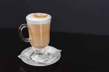 Koyu ahşap arka planda, büyük bardakta kahve macchiato. Camın yanında kopyalamak için yer var ve fotoğraf yatay.