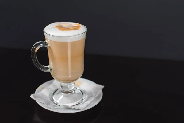 Koyu ahşap arka planda, büyük bardakta kahve macchiato. Camın yanında kopyalamak için yer var ve fotoğraf yatay.