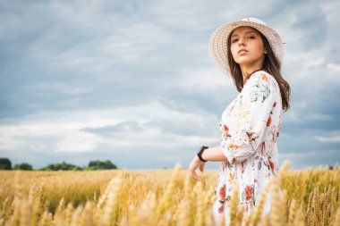 Buğday tarlasında bir kızın portresi. Buğday tarlasında beyaz elbiseli ve şapkalı güzel bir kızın portresi. Beyaz elbiseli ve şapkalı kız. Buğday tarlası. Doğada genç bir kadının portresi.