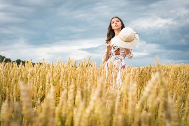 Buğday tarlasında bir kızın portresi. Buğday tarlasında beyaz elbiseli ve şapkalı güzel bir kızın portresi. Beyaz elbiseli ve şapkalı kız. Buğday tarlası. Doğada genç bir kadının portresi.
