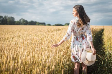 Genç, duygusal, açık renk elbiseli güzel bir kız. Gün batımında açık renk şapkalı, altın bir tarlada.