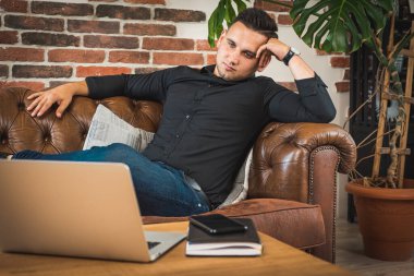 Çoklu görev. Siyah gömlekli ve kotlu yakışıklı bir adam kanepede yatıyordu. Masanın üzerinde dizüstü bilgisayarını açmıştı. Ofiste çalışıyordu.