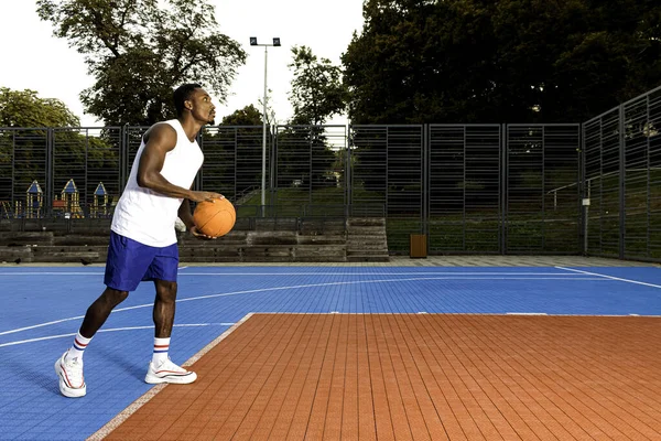Young african american basketball player in white t-shirt and blue shorts on basketball court having fun, throwing basketball, conceived, sports concept, healthy movement.