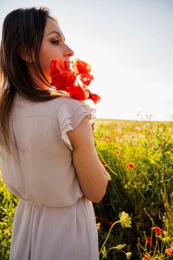 Açık renk elbiseli, elinde kırmızı gelinciklerle altın saat çiçekli çayırlarda gezen sakin yaz manzarası, romantik ruh hali, farkındalık, doğa, özgürlük, yaşam tarzı