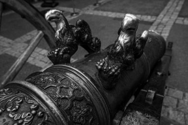 Süslü detayları olan antik bir bronz topun yakın çekimi. Tarihi bir topçu parçasında dekoratif kartal figürleri ve karmaşık desenler sergileniyor.