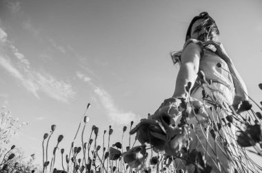 Uçsuz bucaksız gökyüzünün altındaki haşhaş tarlasında bir kadının doğayla olan özgürlük ve bağını yakaladığı düşük açılı, siyah beyaz bir görüntü.