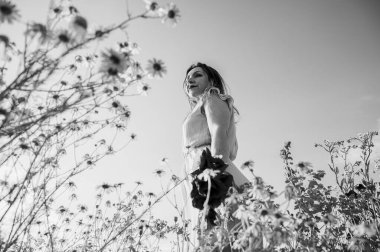 Uçsuz bucaksız gökyüzünün altındaki haşhaş tarlasında bir kadının doğayla olan özgürlük ve bağını yakaladığı düşük açılı, siyah beyaz bir görüntü.