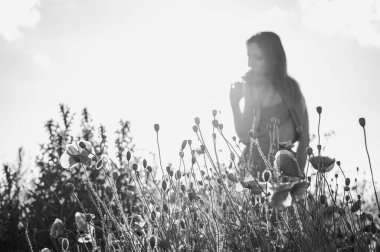 Uçsuz bucaksız gökyüzünün altındaki haşhaş tarlasında bir kadının doğayla olan özgürlük ve bağını yakaladığı düşük açılı, siyah beyaz bir görüntü.