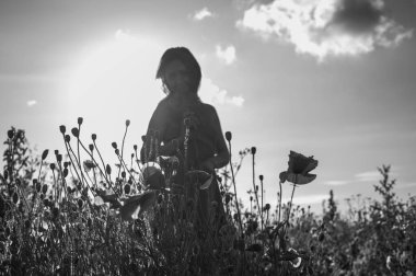 Uçsuz bucaksız gökyüzünün altındaki haşhaş tarlasında bir kadının doğayla olan özgürlük ve bağını yakaladığı düşük açılı, siyah beyaz bir görüntü.