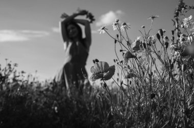 Uçsuz bucaksız gökyüzünün altındaki haşhaş tarlasında bir kadının doğayla olan özgürlük ve bağını yakaladığı düşük açılı, siyah beyaz bir görüntü.
