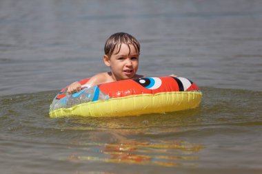 Şişme lastik çemberli mutlu küçük çocuk suyun üzerinde eğleniyor. Lastik halkalı çocuk