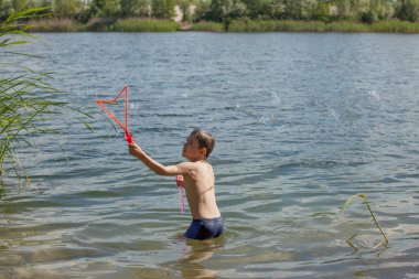 Küçük çocuk gölde sabun köpüğü üflüyor.