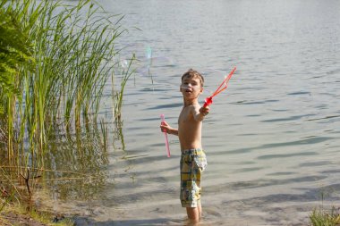 Küçük çocuk gölde sabun köpüğü üflüyor.