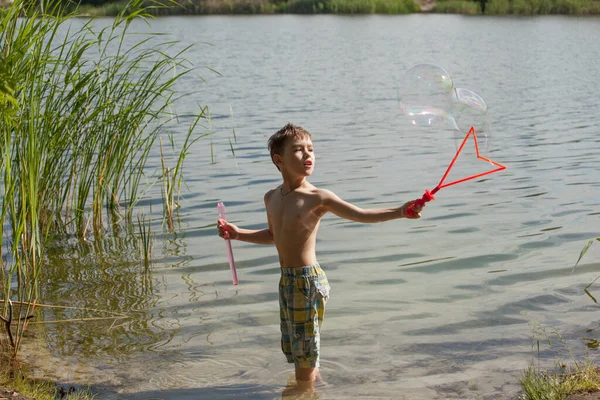 Mały Chłopiec Dmuchający Bańki Mydlane Nad Jeziorem — Zdjęcie stockowe