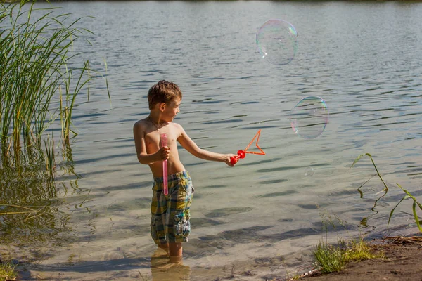 Mały Chłopiec Dmuchający Bańki Mydlane Nad Jeziorem — Zdjęcie stockowe