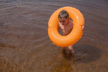 Küçük çocuk şişme bir çemberle nehirde yüzüyor.