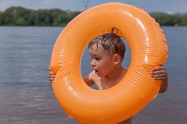 Küçük çocuk şişme bir çemberle nehirde yüzüyor.