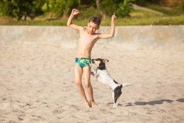 Çocuk deniz sahilinde bir köpekle oynuyor.