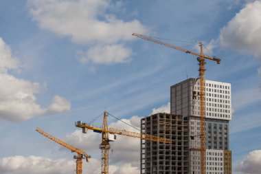 Mavi gökyüzüne karşı kümülüs bulutlu vinçleri olan inşaat alanı