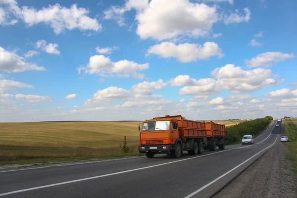 Country road against the blue sky in summer. Lorry with a trailer on a country road