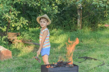Barbeküye yakın hasır şapkalı küçük çocuk.