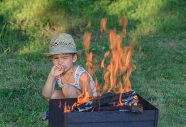 Barbeküye yakın hasır şapkalı küçük çocuk.