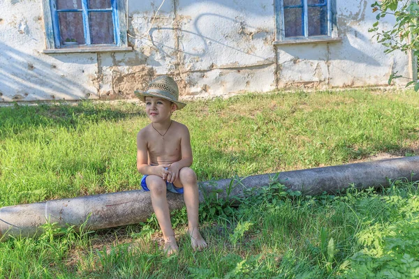 Kleiner Junge Mit Strohhut Sitzt Auf Einem Baumstamm Vor Dem — Stockfoto