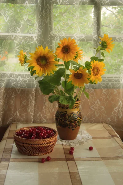 Still life with a bouquet of sunflowers in a vase, cherries and apples