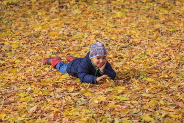 Sonbahar parkında yapraklardan bir halının üzerinde yatan mutlu çocuk.
