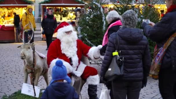 Eine ältere Frau sitzt glücklich auf dem Weihnachtsmann-Schoß auf dem Weihnachtsmarkt. — Stockvideo