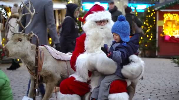 A little boy is happy to sit on Santas lap at the Christmas fair. — Stock Video