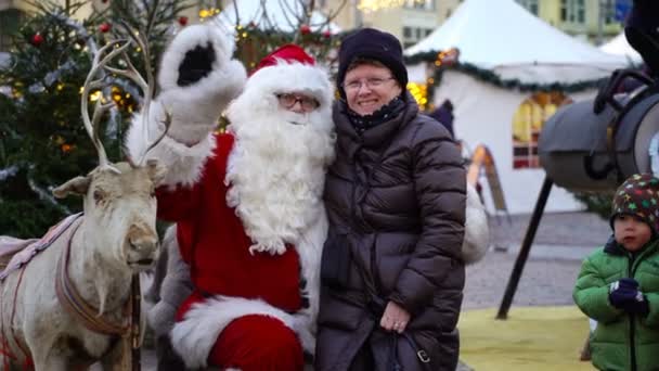 Eine ältere Frau sitzt glücklich auf dem Weihnachtsmann-Schoß auf dem Weihnachtsmarkt. — Stockvideo