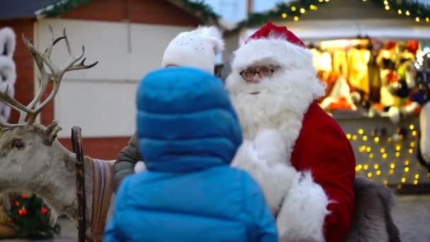 Une petite fille est heureuse de s'asseoir sur les genoux du Père Noël à la foire de Noël . — Video