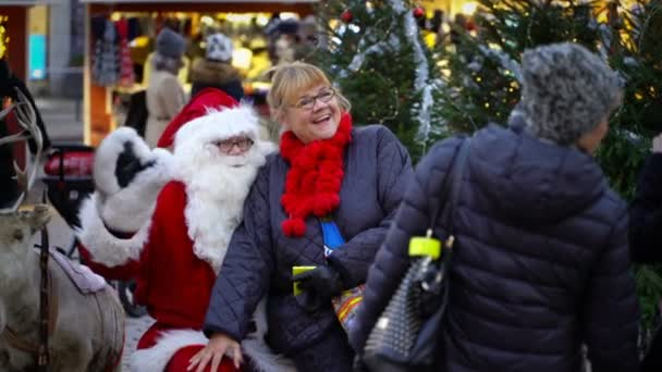 Starsza kobieta jest szczęśliwy, aby siedzieć na kolanach Santas jarmarku bożonarodzeniowym. — Wideo stockowe