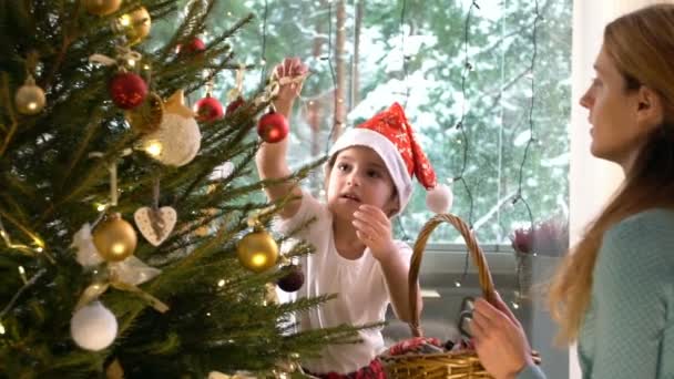 Liten söt flicka med sin mamma dekorera julgran — Stockvideo