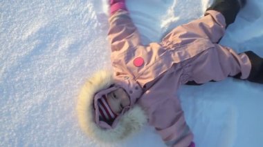 Küçük kız karda soğuk güneşli bir günde yalan bir kar melek yapar