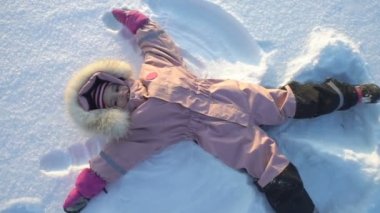 Küçük kız karda soğuk güneşli bir günde yalan bir kar melek yapar