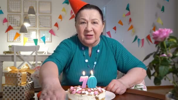 Счастливая пожилая женщина держит торт в руках, когда празднует день рождения со своей семьей через видеочат — стоковое видео